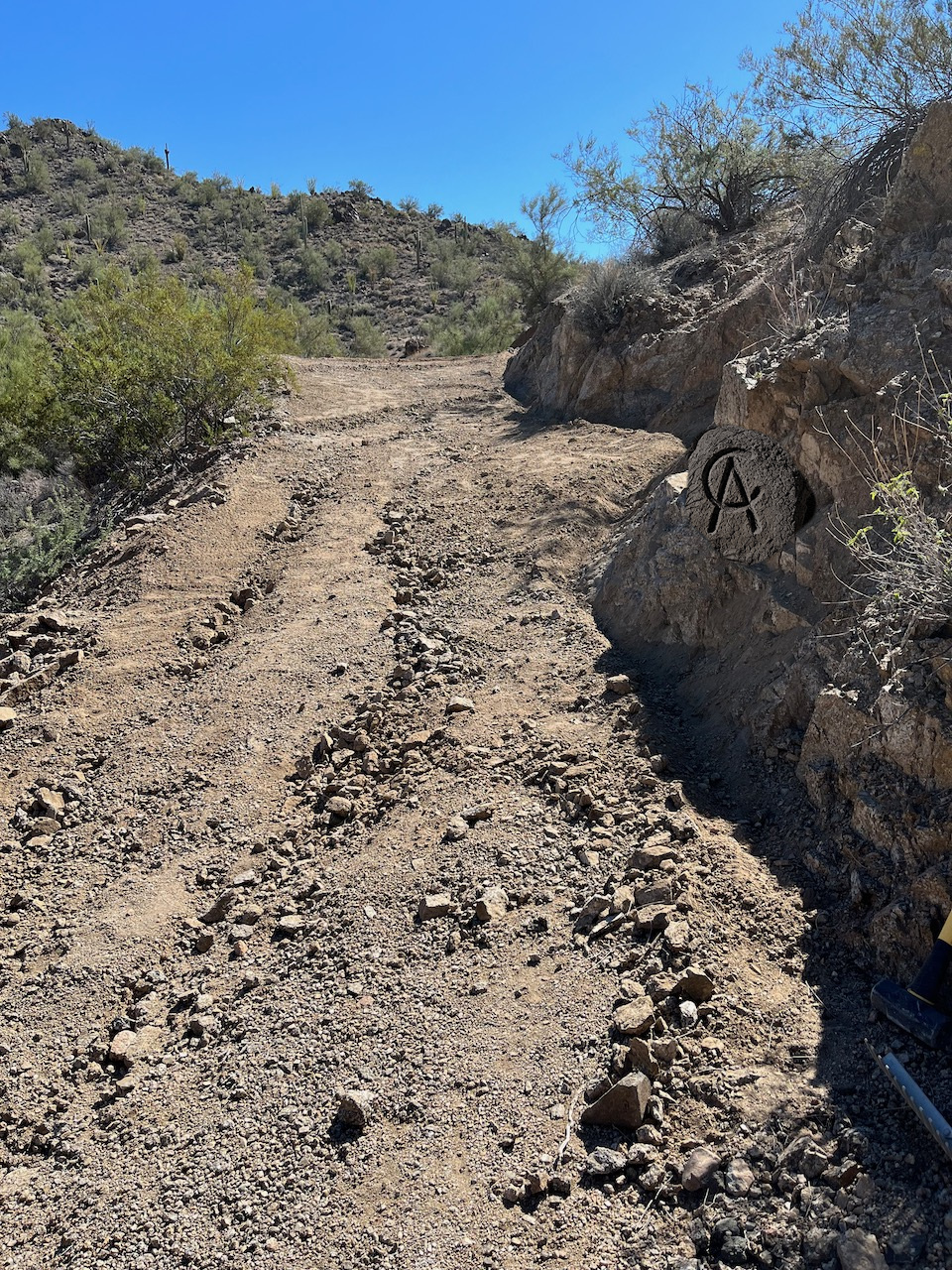 A red-dirt road bending into a desert canyon at dusk, CA brand carved in the rocks